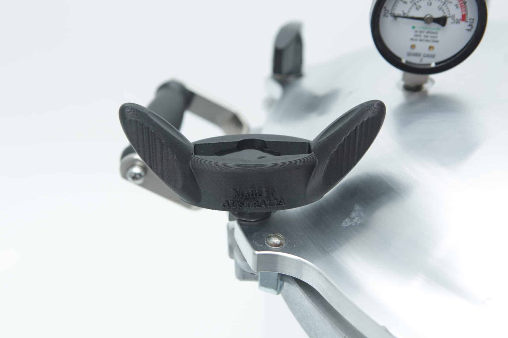 Close-up of an All American Tool pressure cooker lid featuring a black handle and pressure gauge, set against a white background.