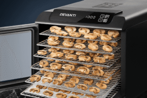 The Devanti 6 Trays Food Dehydrator with stainless steel trays is shown drying sliced mushrooms on a sleek black marble surface.