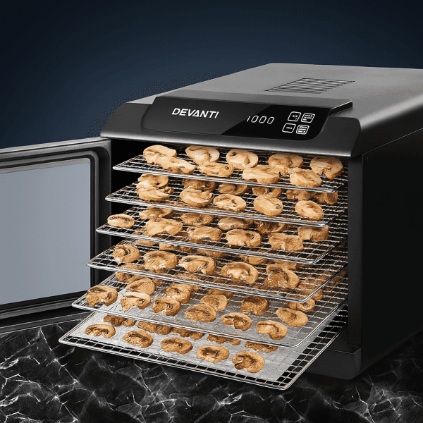 The Devanti 6 Trays Food Dehydrator with stainless steel trays is shown drying sliced mushrooms on a sleek black marble surface.