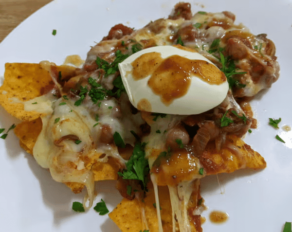 How to Cook any Mushroom? 2 Nachos topped with melted cheese, beans, salsa, soured cream, and savoury cooking mushrooms, garnished with chopped parsley on a white plate.