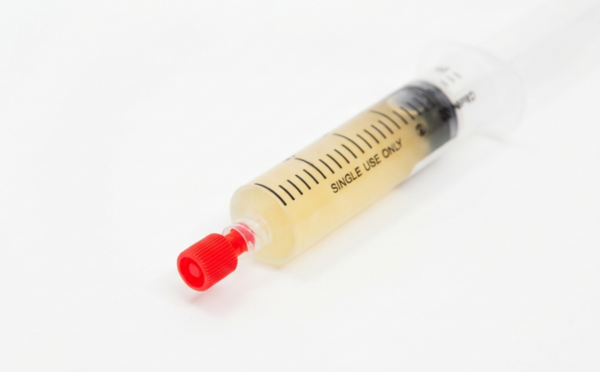 A syringe filled with a yellowish liquid, capped with a red sterile syringe cap, rests on a white background.