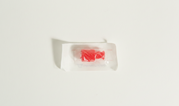 A single red hard sweet in a clear plastic wrapper, resembling a sterile syringe cap, sits on a white background.