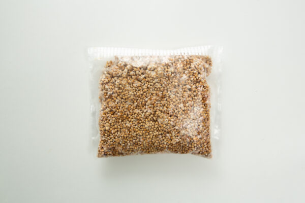 A sealed plastic bag filled with small, round, light brown grains on a white background.