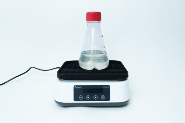 A clear flask with liquid sits on an electronic laboratory stirrer with a digital display.