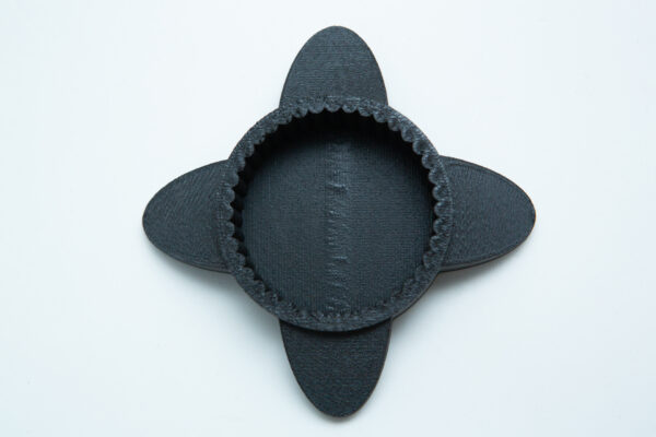 A round, black, 3D-printed object with four oval flaps, placed on a white background.