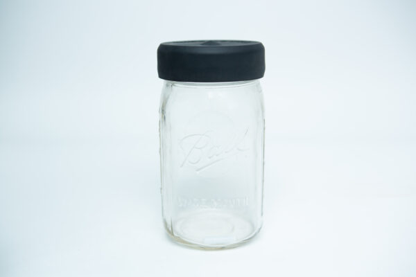 An empty clear glass Kilner jar with a silicone Kilner jar rubber lid (wide mouth), black in colour, sits on a white background.