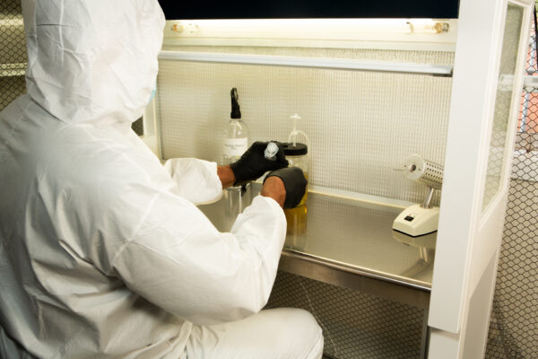 A person in protective gear works with lab equipment and liquids inside a sterile laboratory fume cupboard.