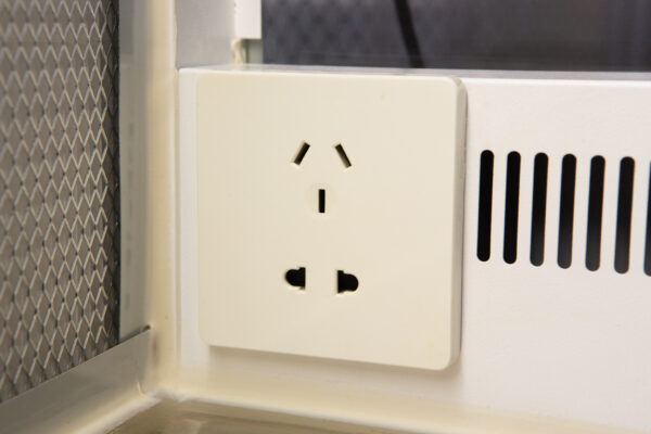 A close-up of a white electrical power socket on a wall, with three plug slots visible.