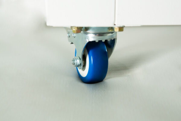 Close-up of a blue castor wheel attached to the bottom of a white piece of furniture on a light surface.