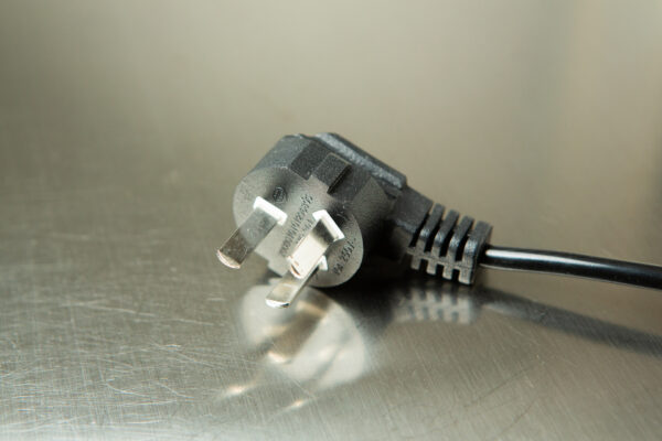 Close-up of a black three-pin electrical plug on a metallic surface.
