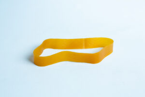 A single yellow elastic band lies flat on a light blue surface.